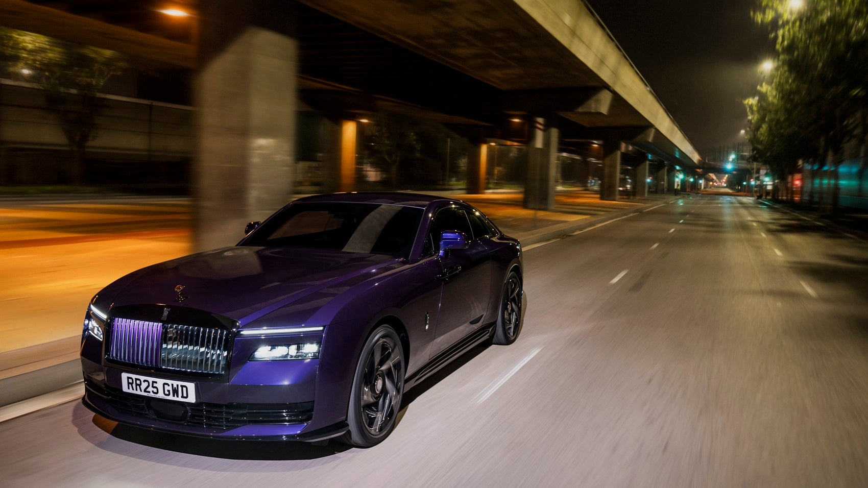 Un elegante Rolls-Royce Black Badge Spectre de color morado circulando por una calle de Baltimore por la noche